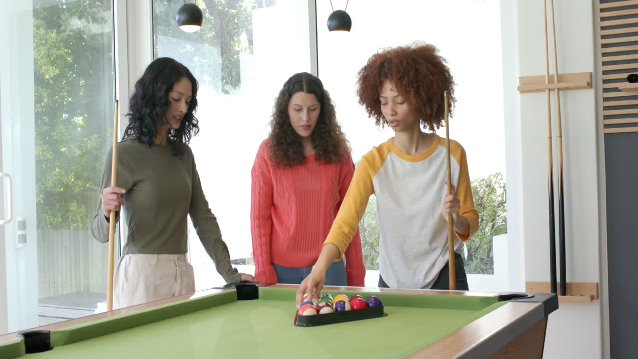 Diverses amies regardant le râtelier, arrangeant les boules et plaçant la bille blanche sur la table de billard pour jouer