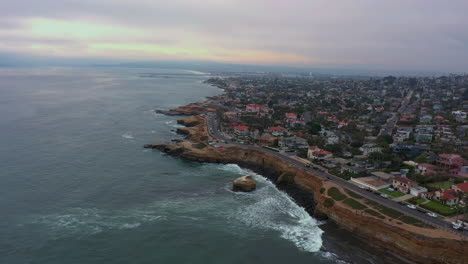 aerial view of waves crashing on cliffs with coastal community of sunset cliffs in the point loma, san diego, california