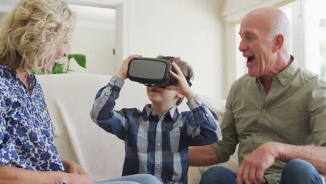 Happy-senior-caucasian-couple-with-grandson-using-vr-headset-in-living-room