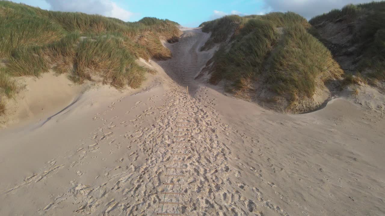 una toma estática de un avión no tripulado captura los poderosos vientos que arrastran la arena a través de las dunas en la playa de hvide sande, con cielos tormentosos y costa accidentada que establece la escena dramática en un día de viento en dinamarca