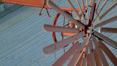 rust coloured spinning windmill with tin roofs in the background