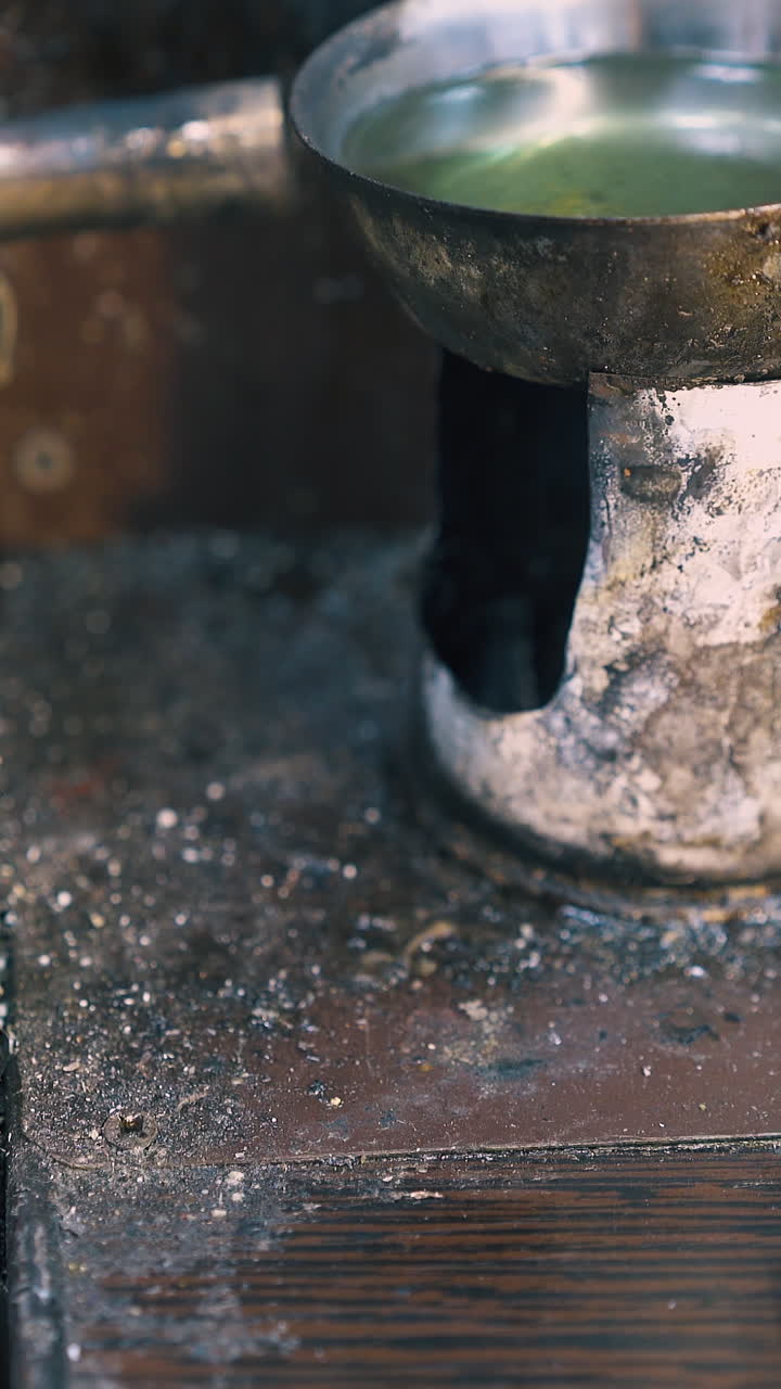 CU shot: professional jeweler installs gas burner on table to heat green liquid in small metal bowl in light workshop closeup