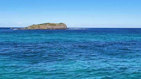 a tranquil island surrounded by clear, vibrant blue ocean under a bright, cloudless sky.