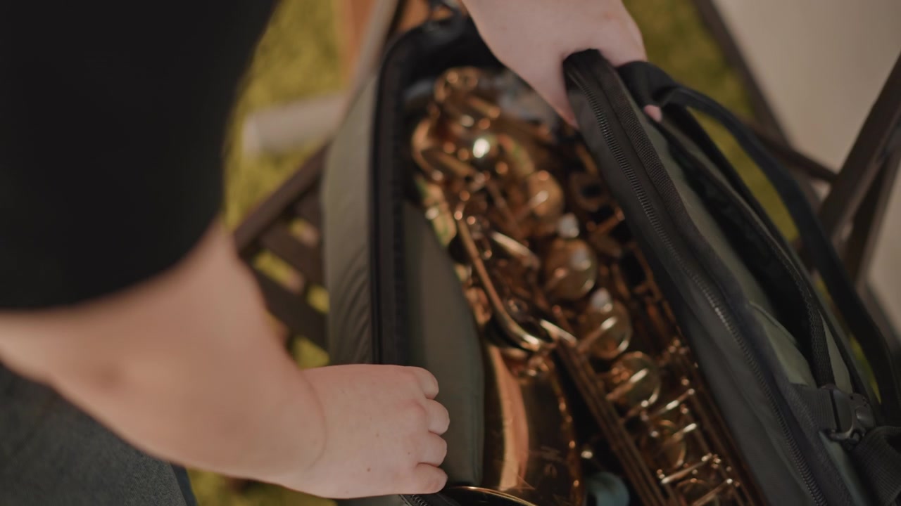 Musicista professionista caucasico che svela il sassofono nella custodia, mani ferme aprono la pesante custodia, chiavi dorate catturano la luce, ispezione delle chiavi e dei tamponi, preparazione concentrata per la performance, inquadratura ravvicinata.