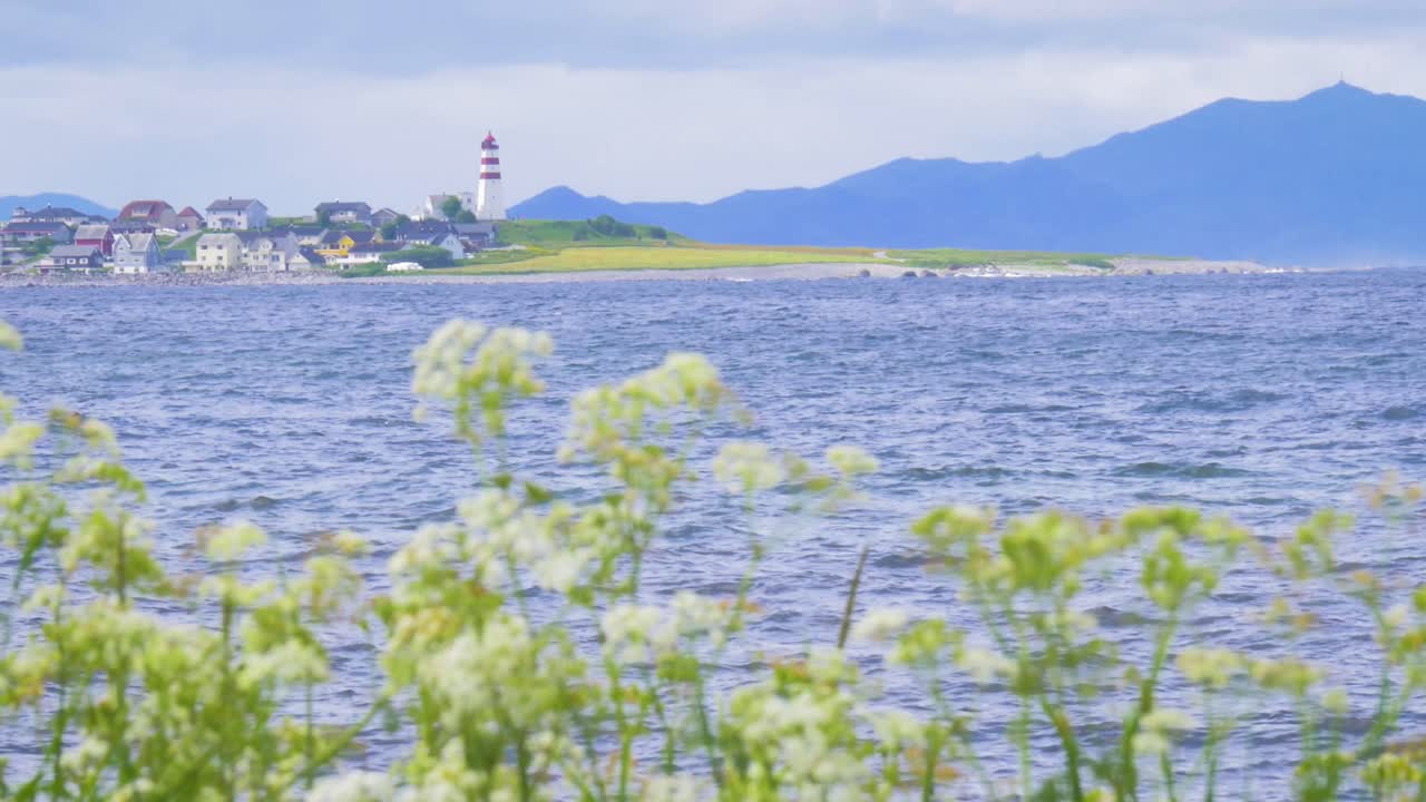 A wide static shot of a lighthouse in Norway. Filmed on a summer day overlooking a calm sea in clear weather.