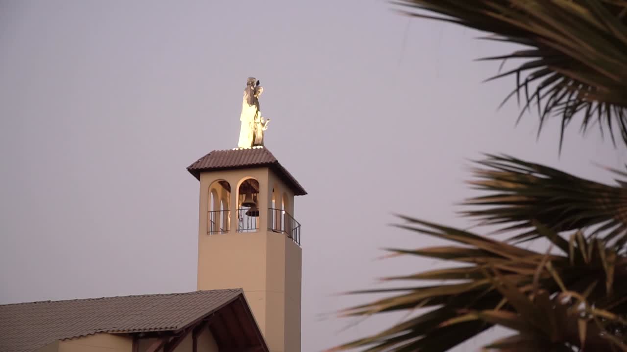 Campanário de igreja e estátua iluminados durante o pôr do sol em La Molina, Lima, Peru