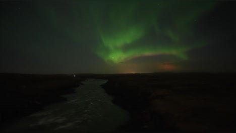 Wide-shot-of-Aurora-Borealis-at-night-sky-and-flowing-river-in-darkness-on-Iceland