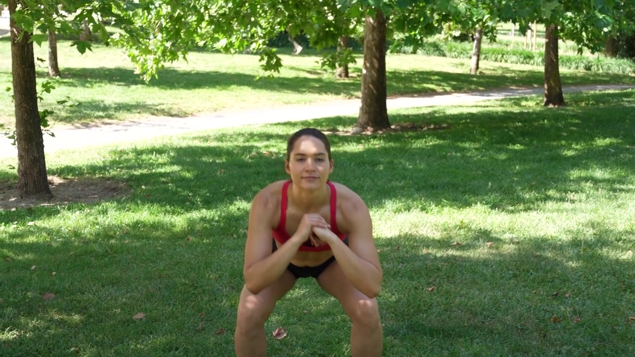 Una donna si allena all'aperto facendo squat in un parco per migliorare la sua forma fisica e la sua forza.