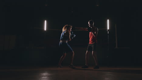 Female-boxer-punching-a-focus-mitts-with-boxing-gloves-in-a-smoky-gym