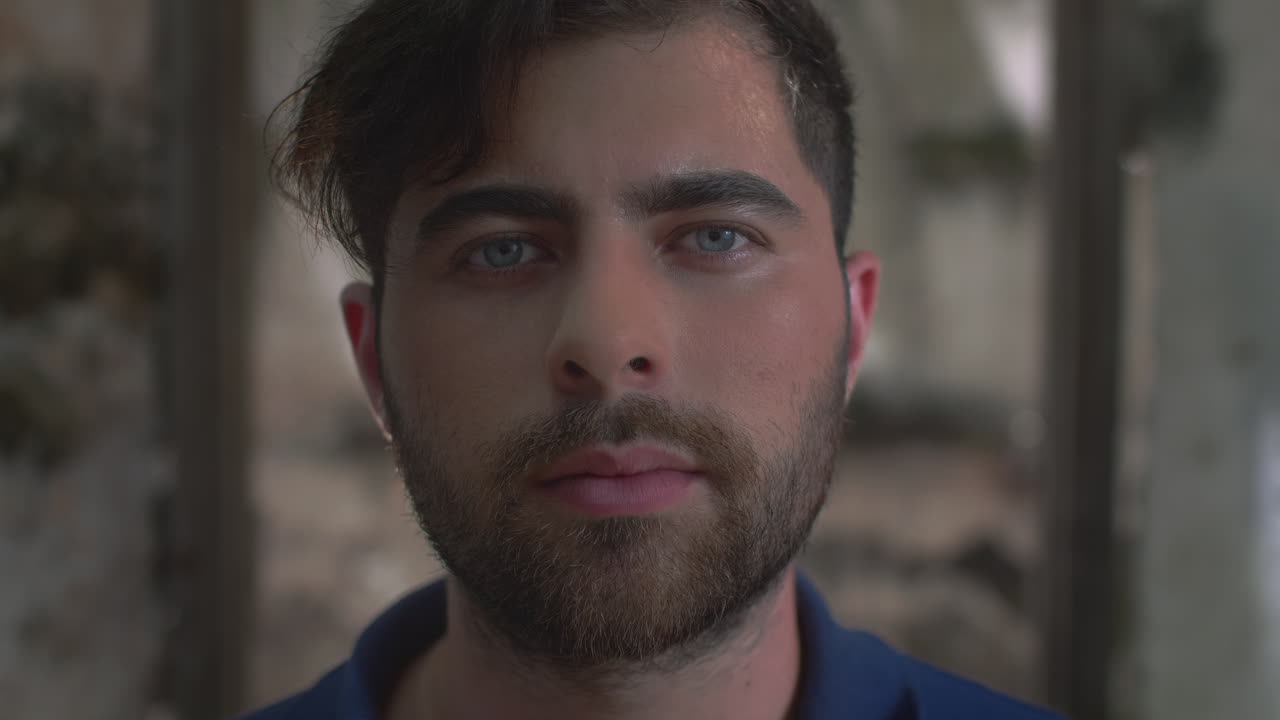 High-quality 4K footage of a focused young man with blue eyes and a beard, slowly opening his eyes in a cinematic outdoor setting. Ideal for travel, identity, mystery, or emotional