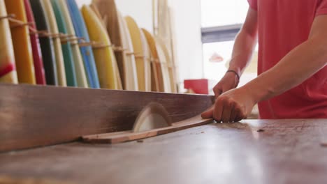 fabricante de tablas de surf masculino caucásico trabajando en su estudio y haciendo una tabla de surf de madera