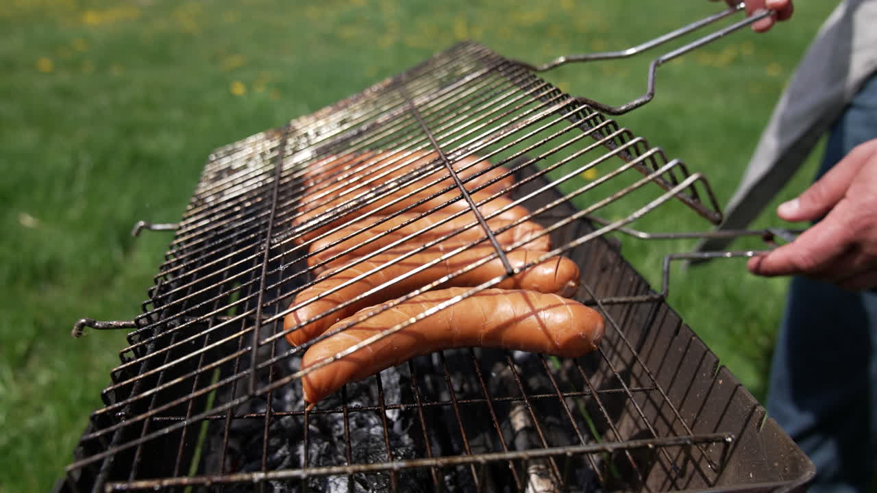 Barbeque sausages grilling for picnic. Man holding on fire roasted meat.