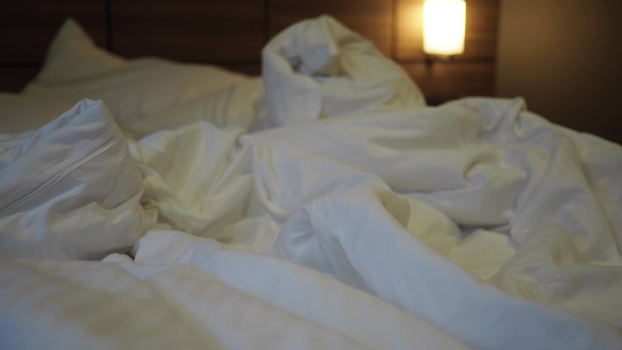 Tempat Tidur yang Belum Dirapikan dengan Seprai Putih dan Bantal di Kamar Tidur yang Nyaman