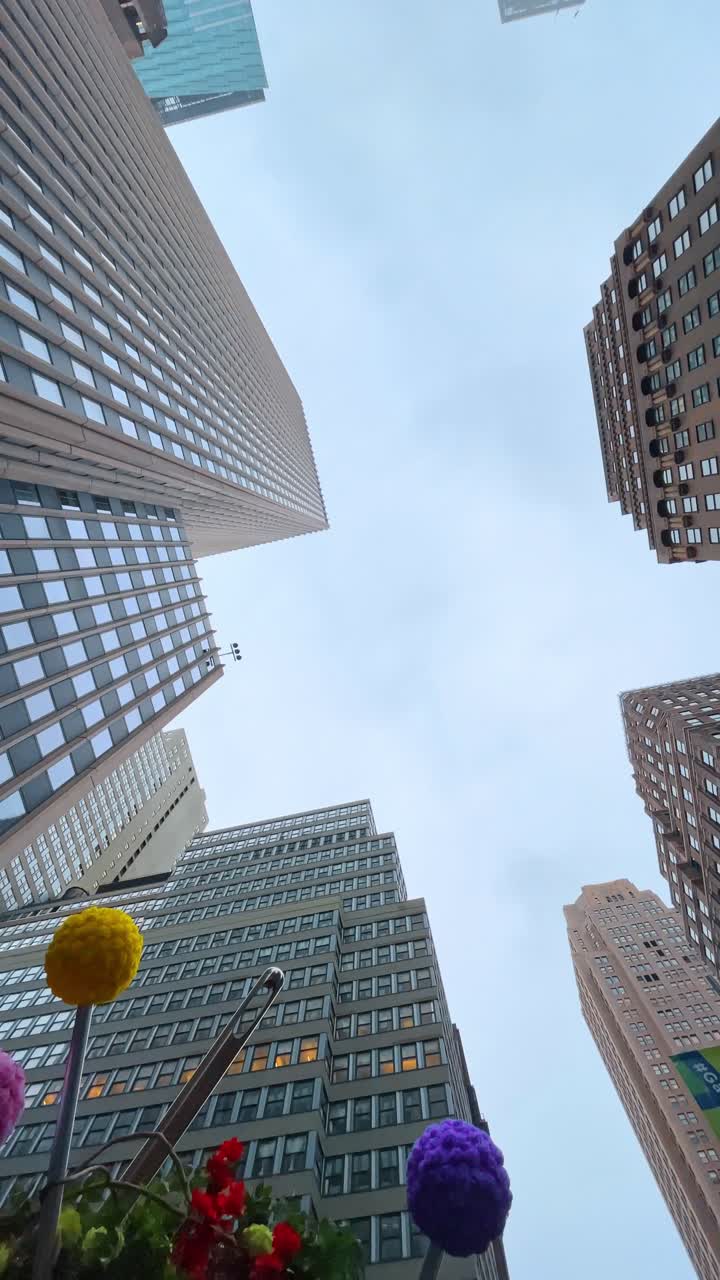 New York, USA, 11 May 2025: Worm's eye view of skyscrapers and decorative floral elements. Directly upward view of modern office buildings in New York with colorful artificial flowers