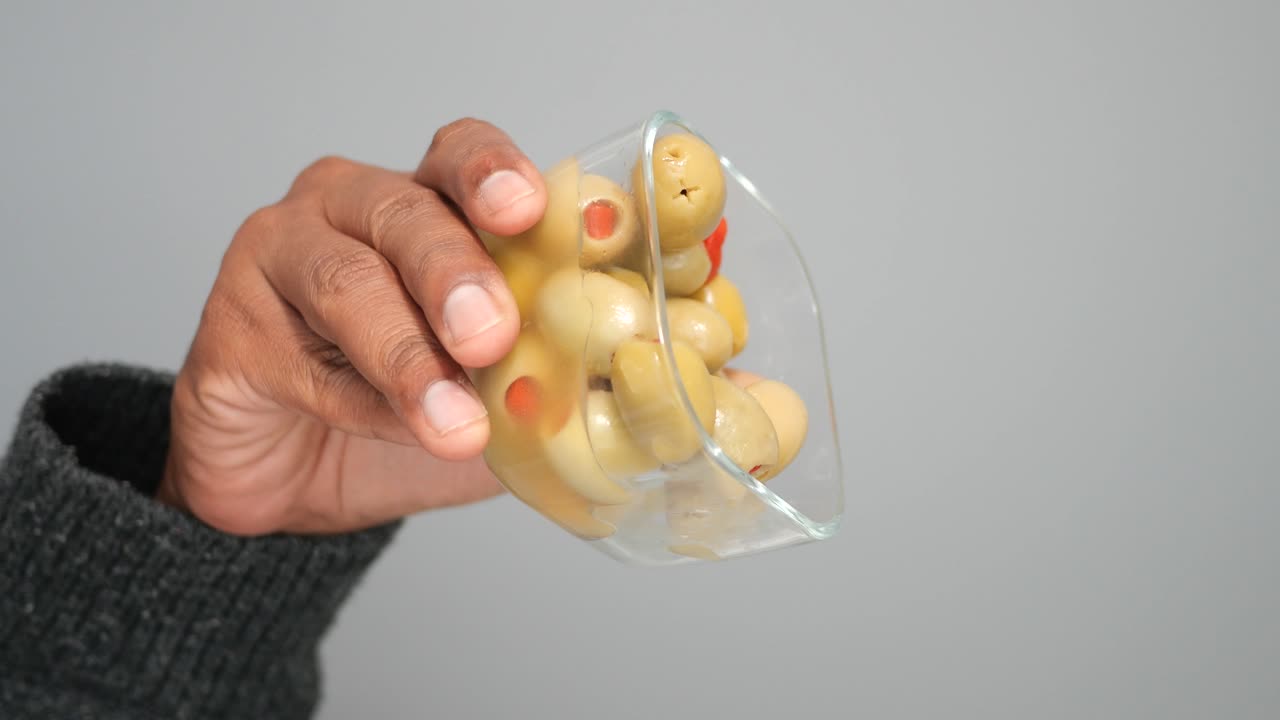 A hand holding a glass filled with green olives