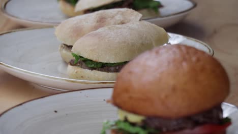 a chef places a cooked and assembled meat hamburger with lettuce, tomato, and cheese on a plate