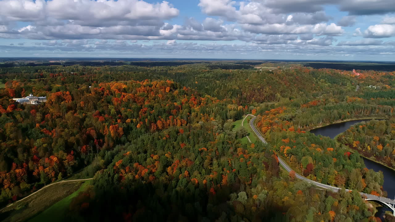 toma aérea hacia atrás del hermoso paisaje forestal con árboles coloridos con río, puente y nubes en el cielo