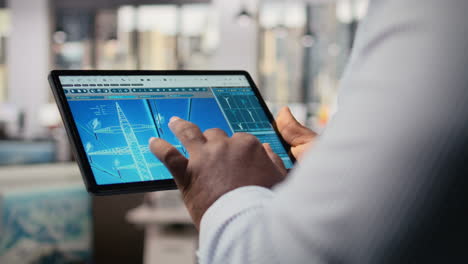 close up of engineer using tablet to design power line towers in office