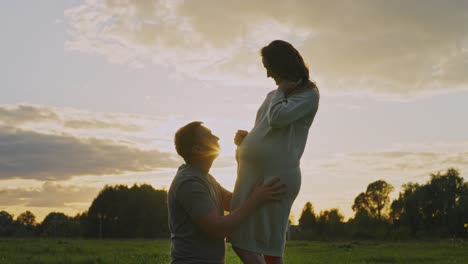 man kissing pregnant woman's belly at sunset