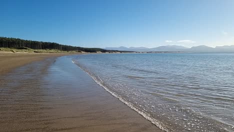 hazy snowdonia mountain range across idyllic slow motion shimmering irish seascape from newborough beach nature reserve