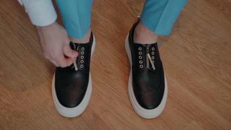 man in blue trousers tying black sneakers with white soles, preparing for a casual event