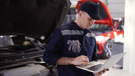 car mechanic working on laptop in auto repair service, lean on a car