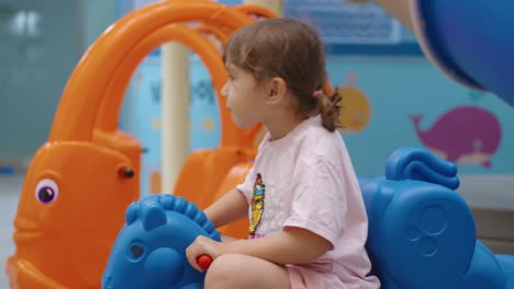 young caucasian white child playing on rocking horse in an indoor play area, bouncing in a colorful environment, tracking sideview in slow motion