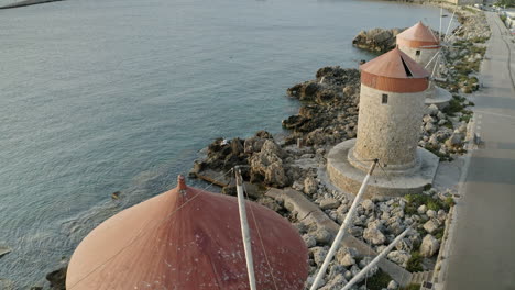 Eine-Luftaufnahme-Der-Stadt-Rhodos-In-Griechenland-Mit-Ausschnitten-Der-Mittelalterlichen-Altstadt,-Dem-Alten-Leuchtturm-Am-Hafen,-Alten-Windmühlen,-Stränden-Und-Einem-Atemberaubenden-Sonnenuntergang