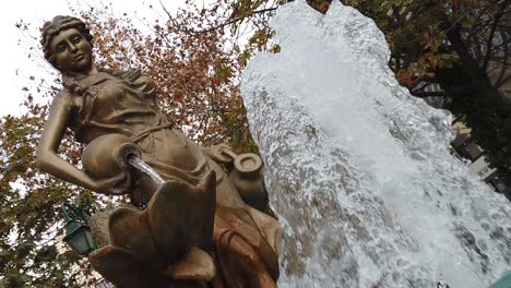 a bronze woman statue behind a fountain