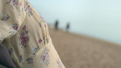 Encantadora-Dama-Descansando-En-La-Playa-De-Arena-De-Pie-Con-Un-Vestido-Florido-Día-Soleado-De-Cerca