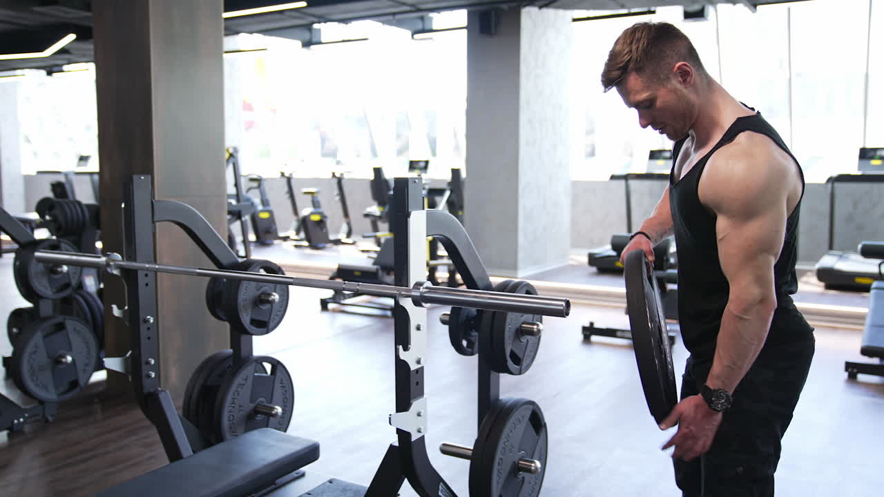 Athletic man in the gym. Muscular man putting heavy plates on barbell and lifting in gym