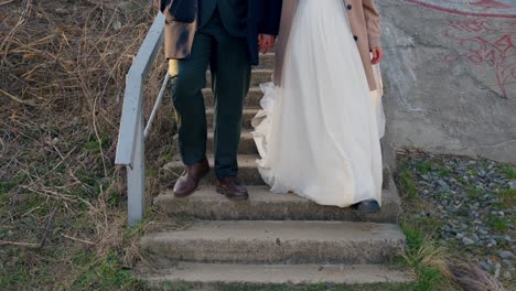 a close-up view of a wedding couple walking down stairs after their ceremony, showing their intertwined hands and elegant attire.