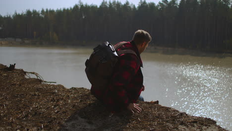 man with backpack comes sits at the lake bank man silhouette wild duck swan is swimming at the lake overgrown bank green reed sun reflection. high quality 4k footage