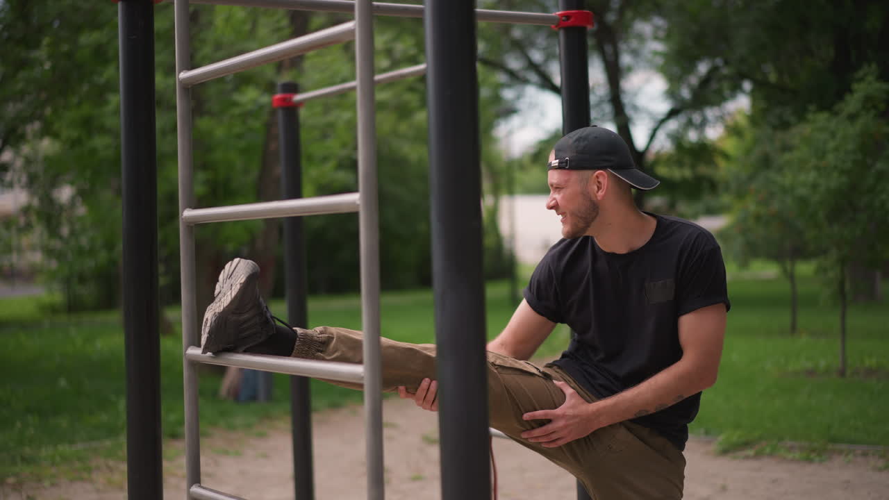 Green Trees Provide Quiet During Workout, Man Prepares On Bars For Functional Hamstring Training Outdoors, Focused Athlete Calmly Stretches Legs On Bar In Green Park Environment Near Trees