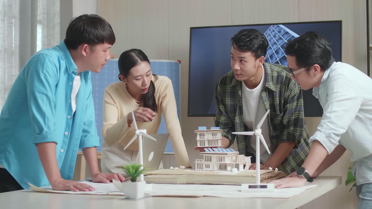 아시아 엔지니어 그룹이 사무실에서 태양 전지판을 가진 작은 집의 모델에 대해 회의를 하고 있습니다.