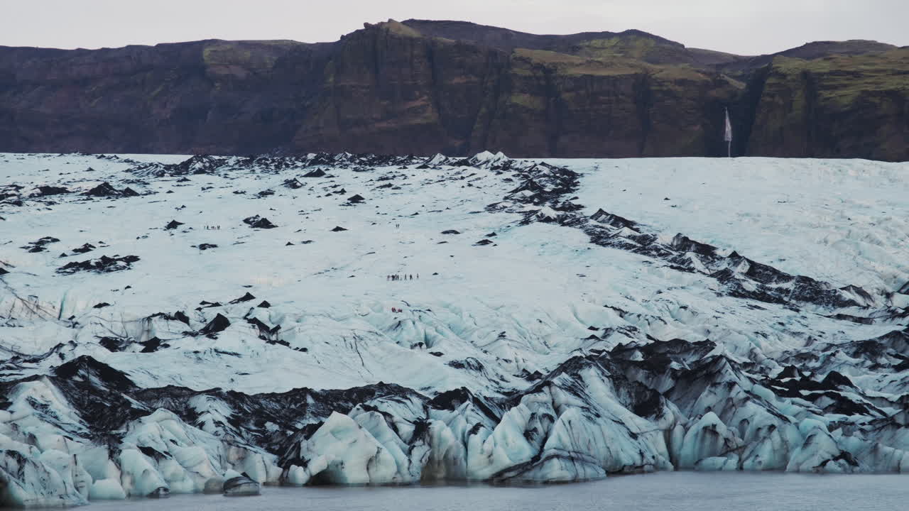 Hikers appear tiny as they explore a vast glacier, navigating the frozen terrain