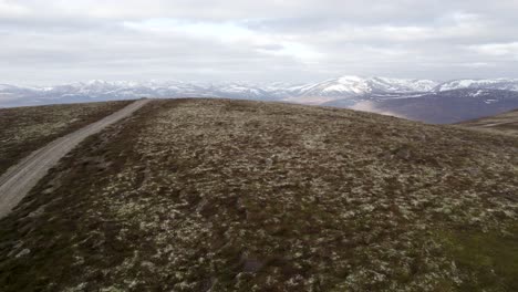 Filmische-Drohnenaufnahmen-Aus-Der-Luft,-Die-Schnell-über-Wildes-Heidekraut,-Moorhuhn-Und-Flechtenheide-Fliegen,-Um-Eine-Berglandschaft-Mit-Schneeflecken-Und-Wolken-Zu-Enthüllen