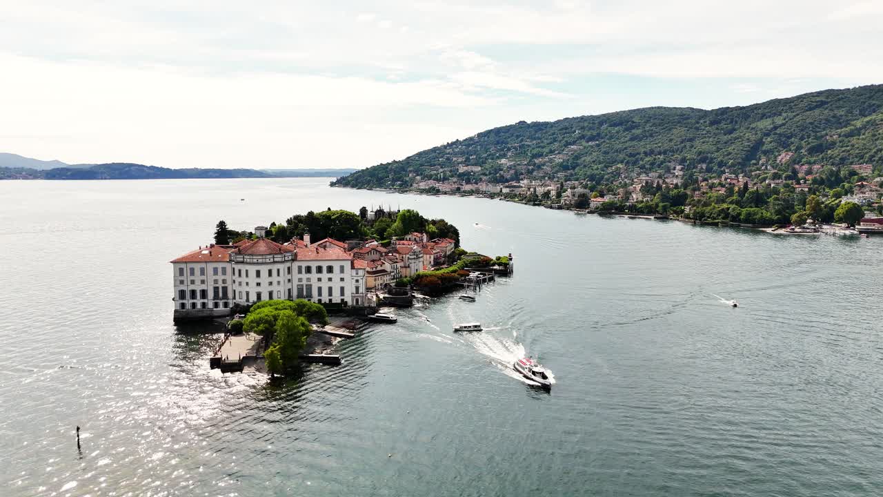 A peaceful view of Sresa on Isola Bella in Italy, featuring a grand waterfront estate, boats moving across calm lake waters, and a lush hillside village stretching along the distant shoreline