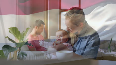 animation of flag of netherlands over caucasian mother feeding baby