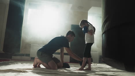 instructor shows child stabile feet position in boxing gym. fighting trainer teaches little girl kickboxing in sports club slow motion. martial arts