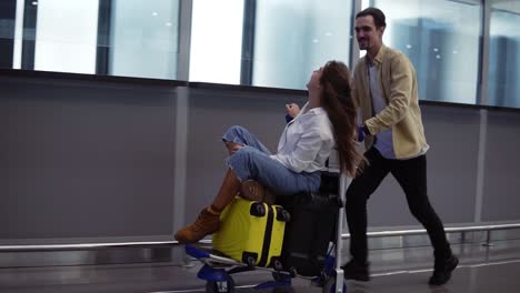 funny couple in airport. attractive young woman and handsome man with suitcases are ready for traveling. having fun on luggage