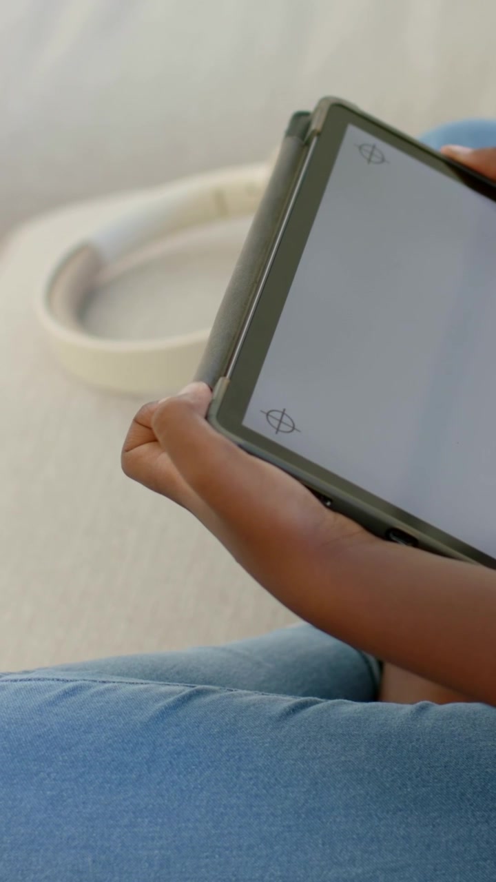 Vertical video: Holding tablet showing cal marks, kid adjusting grip on couch in jeans, headset