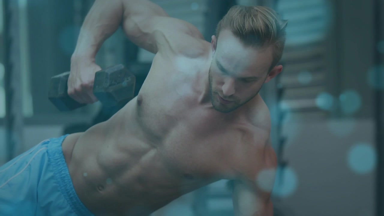 Man bracing forearm, initiating pull with hex dumbbell in gym, blue bokeh highlighting fitness form