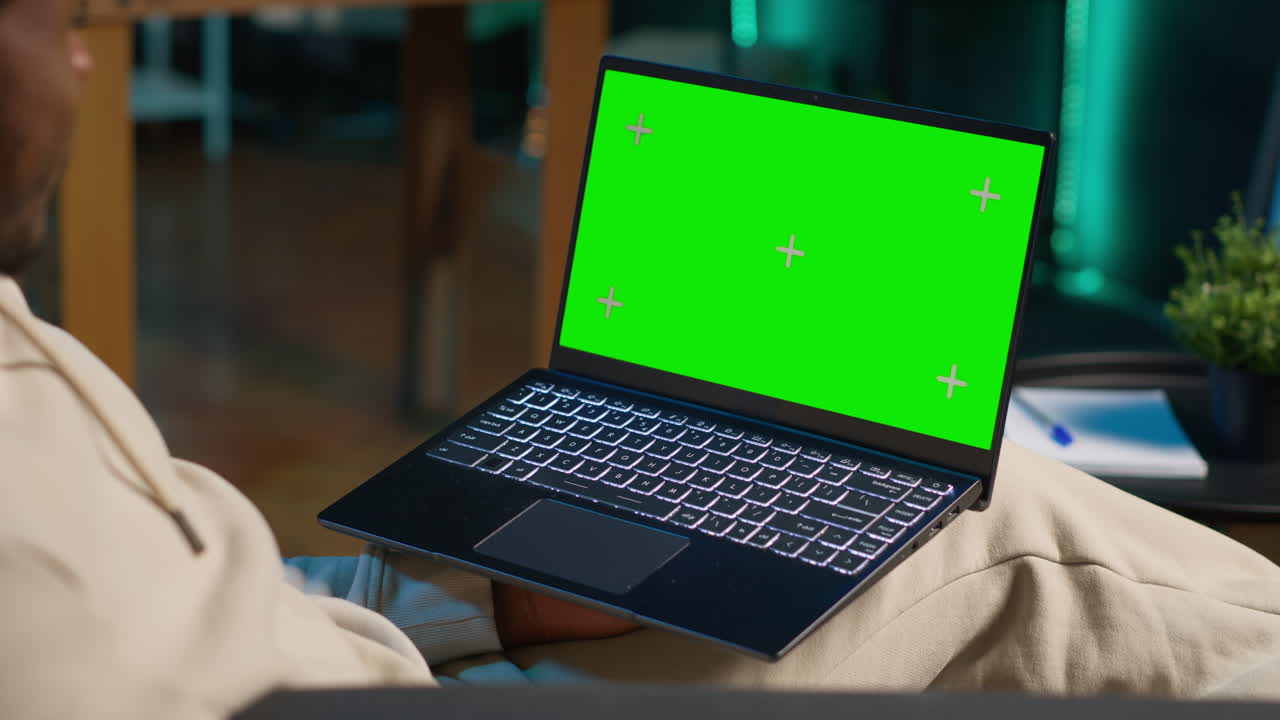 African american remote worker uses chroma key display on device to work from the comfort of his home, sitting on the sofa in his modern stylish living room. Happy young man on internet. Camera A.