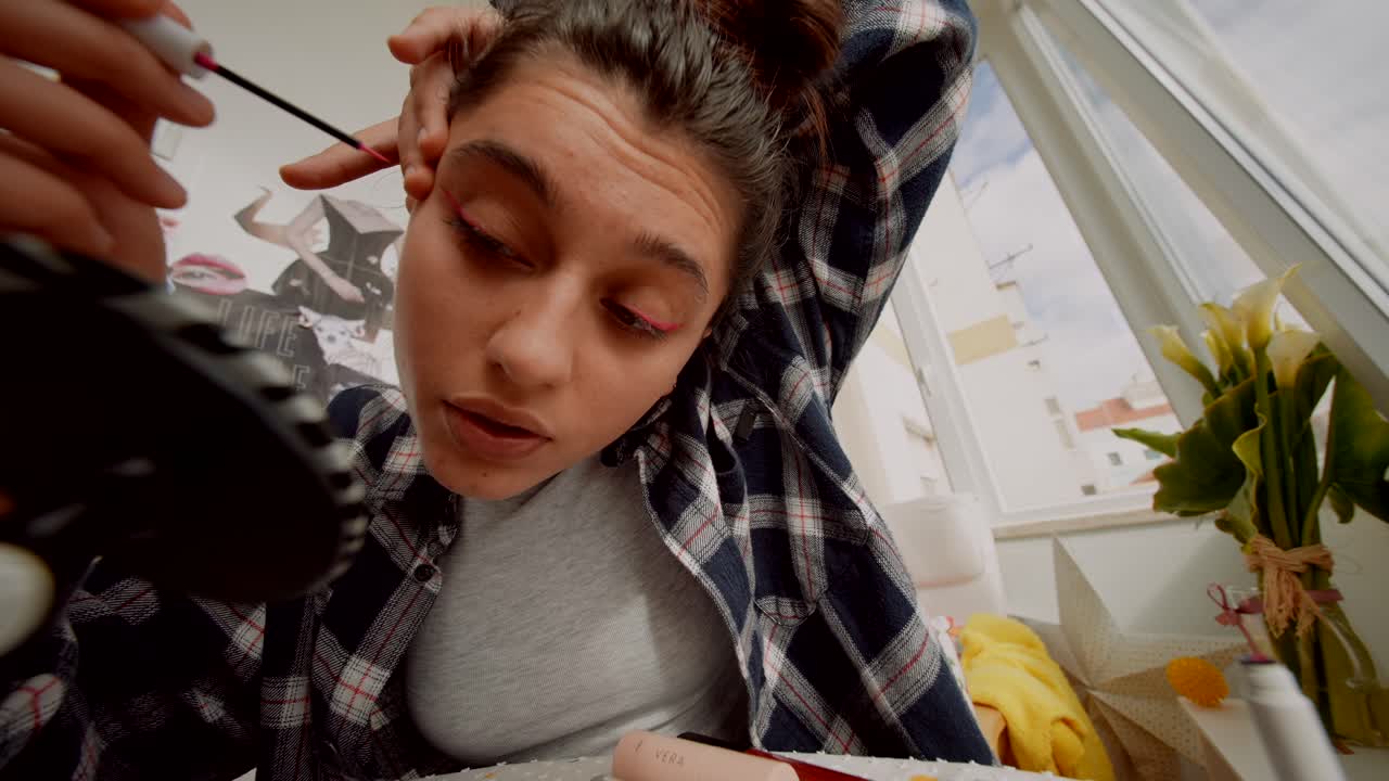 Giovane donna che applica l'eyeliner rosa davanti a uno specchio.