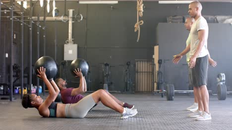 diverse group fitness class training in pairs with medicine balls at gym, in slow motion