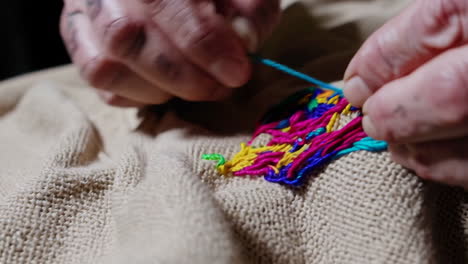 close-up of hands embroidering colorful threads on fabric
