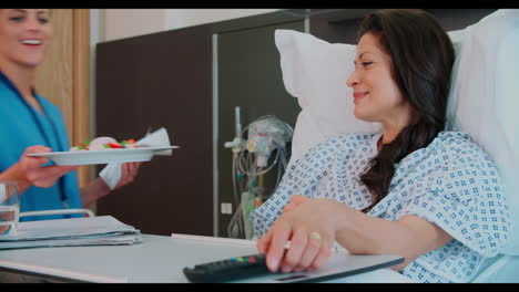 paciente femenina en una cama de hospital siendo servida una comida por ordenado