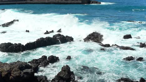 fuertes olas oceánicas chocando contra rocas volcánicas oscuras que se elevan por encima de la superficie, en movimiento lento