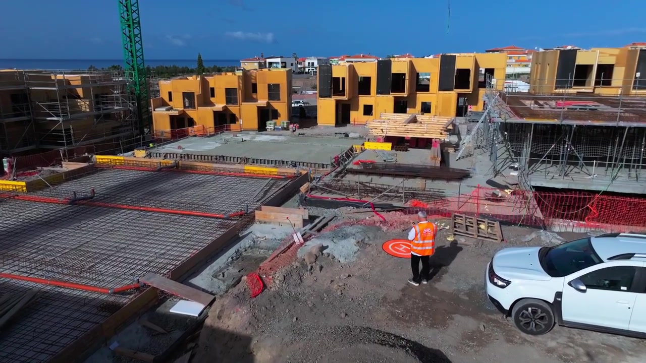 Operador de dron con chaleco de seguridad se prepara para el vuelo en una obra en construcción activa al aire libre.